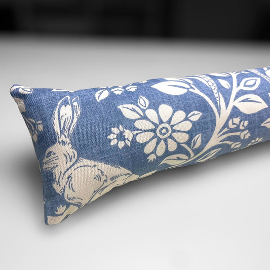 Handmade Blue Woodland Hares draught excluder with a deep blue fabric featuring white hare motifs, placed against a door to block cold air.