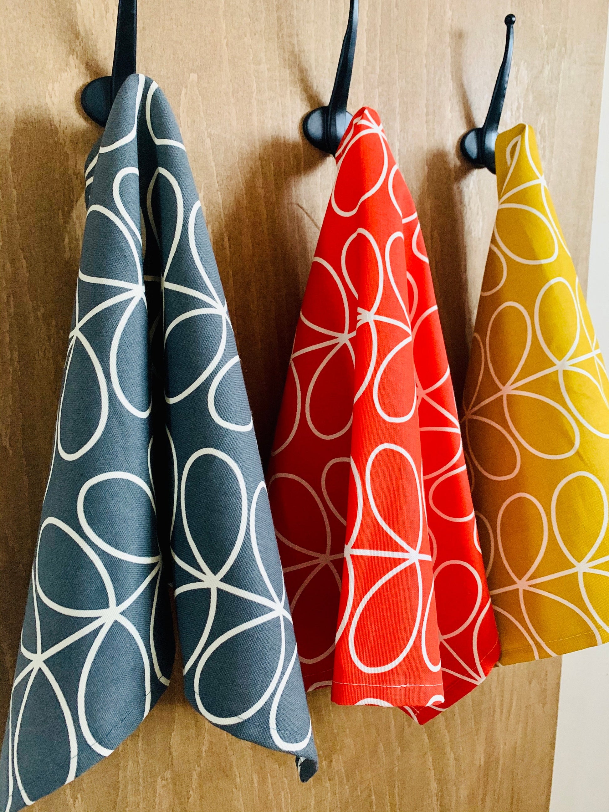 Set of three Orla Kiely kitchen towels featuring a stylish design in grey, red, and yellow. Each towel showcases a distinct retro-inspired pattern, perfect for adding a pop of color and contemporary flair to your kitchen decor.