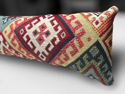 Handmade kilim fabric draught excluder in red, green, and beige tones, designed to block cold air under doors.