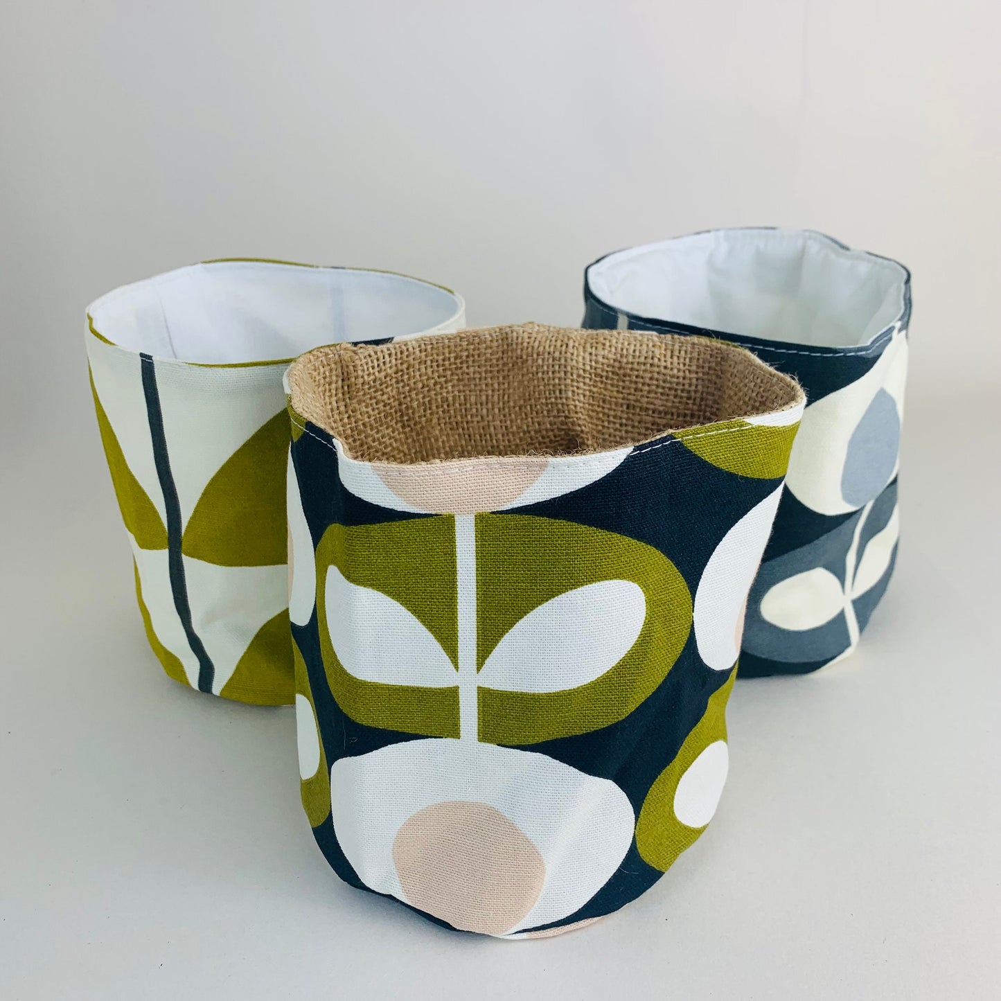 Orla Kiely fabric plant pots and storage baskets in grey and olive, lined with linen or hessian. These versatile containers feature retro-inspired patterns, perfect for adding a stylish touch to your home decor while providing practical storage solutions