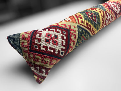 Handmade kilim fabric draught excluder in red, green, and beige tones, designed to block cold air under doors.