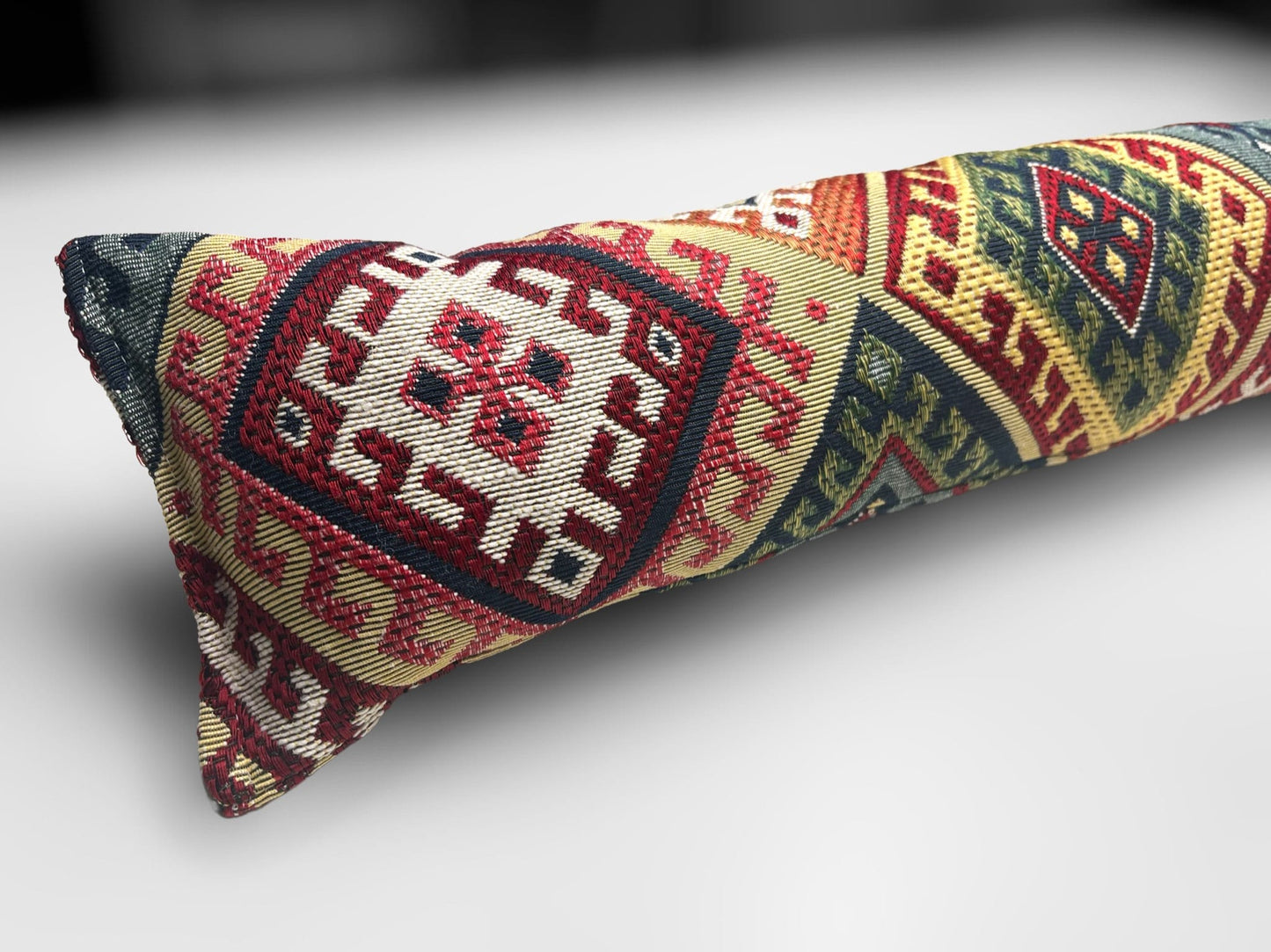 Handmade kilim fabric draught excluder in red, green, and beige tones, designed to block cold air under doors.